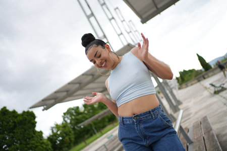 A woman in a blue tank top and blue jeans is dancing in front of a metal structure. She is smiling and she is having funの写真素材