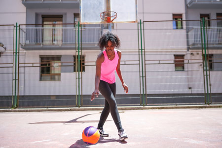 Cute african woman learning to dribble a basketball ball in an urban court aloneの写真素材