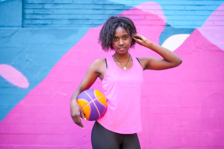Portrait of a beauty african woman holding basketball ball against colorful wall in the cityの写真素材
