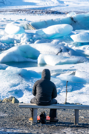 A photographer photographing the floating icebergs in the Jokulsarlon glacier lagoon in Iceland. Wearing a black winter jacketの写真素材