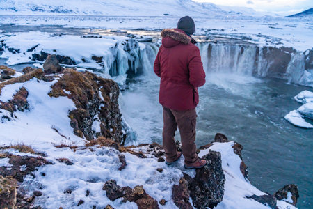 A male hiker looking at frozen Godafoss waterfall at sunset in winter, Iceland.の写真素材