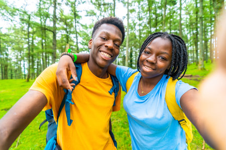 African cheerful young friends embracing taking a selfie in a green forest in springtimeの写真素材
