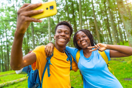 Cheerful african friends taking selfie gesturing victory with hand while hiking in the forestの写真素材