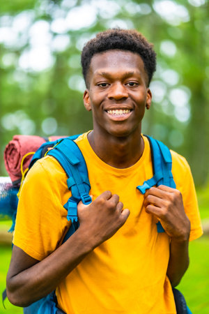 Vertical close-up portrait of a cheerful african backpacker enjoying adventure in natural parkの写真素材