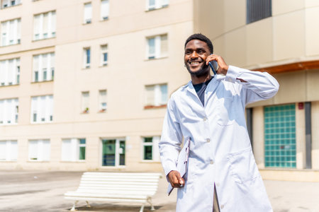 African confident doctor talking to the mobile outdoors next to the hospitalの写真素材