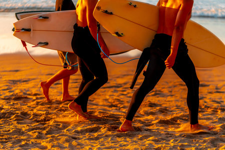 Two men are walking on the beach with surfboards. The surfboards are yellow and white. The beach is sandy and the sky is orangeの写真素材