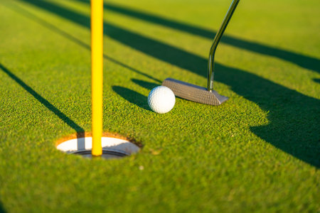 Close-up photo of a golf club, ball and hole in a green golf course