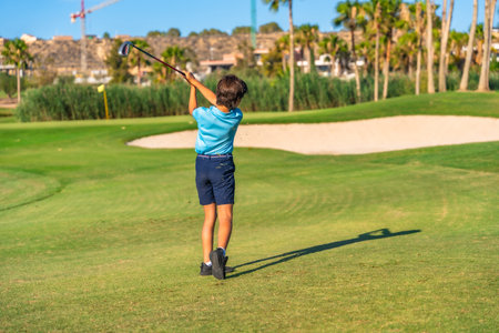 Rear view of an unrecognizable caucasian young boy swinging golf on a green courseの写真素材