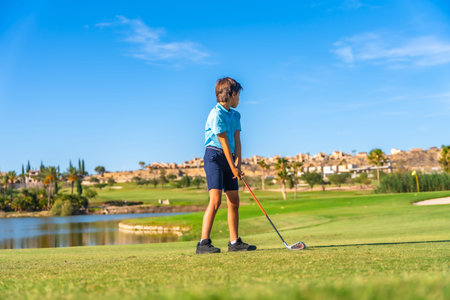 Full length photo of a young caucasian golfer learning to play golf on a course with a pool on a sunny dayの写真素材
