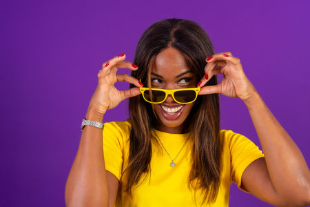Studio portrait with purple background of a confident and playful african woman with sunglassesの写真素材