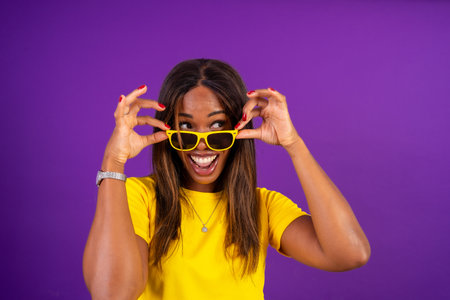 Studio portrait with purple background of a beauty african urban woman playing with sunglassesの写真素材
