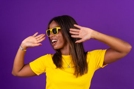 Studio portrait with purple background of an african cool urban woman with sunglasses dancingの写真素材