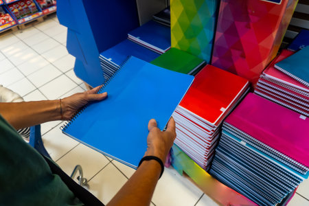A person is holding a blue spiral notebook in a store. The store has many notebooks in different colors and sizes. Back to school conceptの写真素材