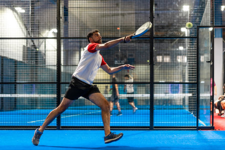 Full length photo of a mature sportive man trying to reach the ball while playing paddle tennis in an indoor courtの写真素材