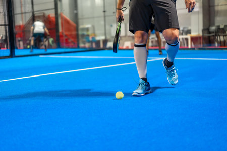 Sportive mature man picking up a paddle ball from the ground in an indoor blue courtの写真素材