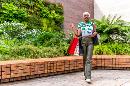Vertical full length photo of a cool african woman walking carrying shopping bags outside a mallの写真素材