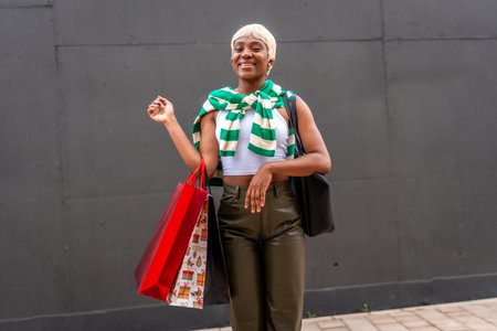 Modern African woman with short hair and casual clothes carrying shopping bags in an urban spaceの写真素材