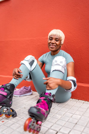 Vertical portrait of a stylish modern african woman smiling sitting on the ground wearing inline...