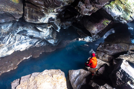 A man sitting in Grjotagja volcanic cave with hot thermal water near Lake Myvatn, Icelandの写真素材