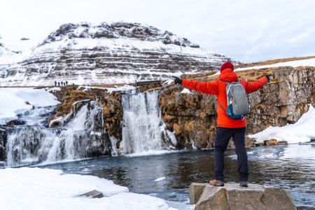 A man with his back turned and his arms open at the waterfall of Mount Kirkjufell in the winter of Icelandの写真素材
