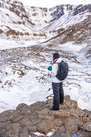A woman hiker with backpack at Hengifoss waterfall in winter Icelandの写真素材