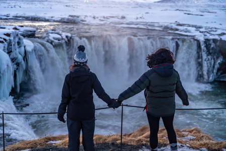 Two people are standing on a ledge looking at a waterfallの写真素材