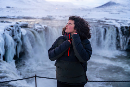 Portrait of a woman at the beautiful Godafoss waterfall in winter in Iceland with her eyes closed.の写真素材