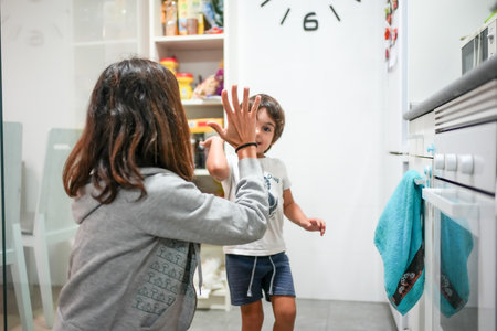 A woman and a child are high fiving each other in a kitchen. The woman is wearing a gray hoodie and the child is wearing a white shirtの写真素材