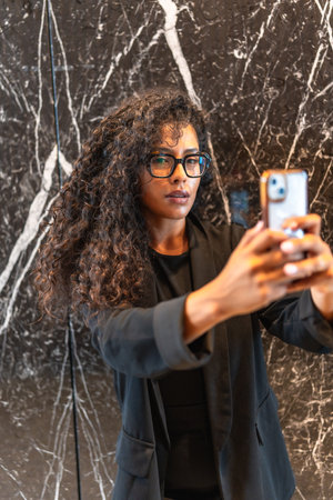 Vertical portrait of a beauty latin businesswoman taking a selfie in a modern buildingの写真素材
