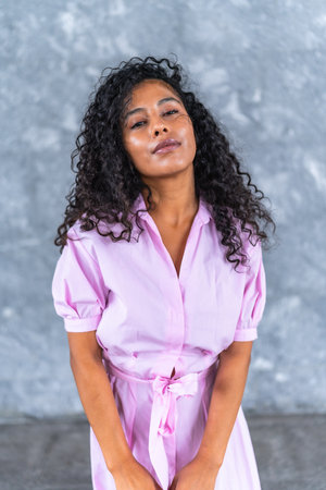 Vertical front portrait against gray urban wall of a chic latin woman in pastel pink elegant clothes posing confidentの写真素材