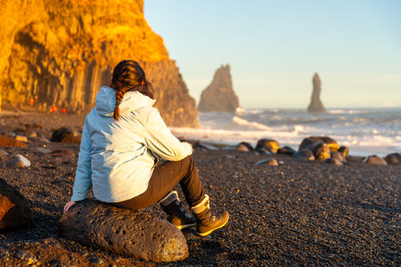Female hiker sitting on the black sand beach of Reynisfjara looking at the sea. Iceland