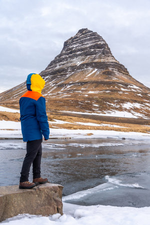 A man with his back turned on Mount Kirkjufell in the cold winter of Icelandの写真素材
