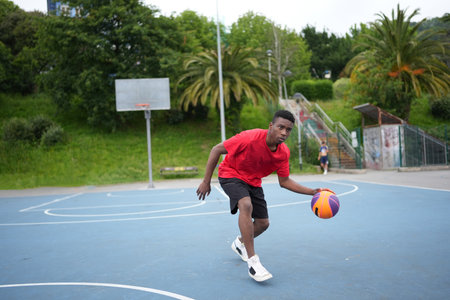 Full length photo of an African American sportive young man playing basketball outdoorsの写真素材