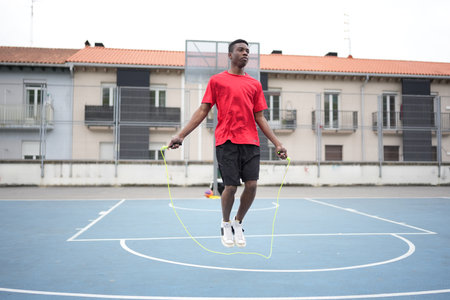 Young African American man wearing sports clothing is jumping rope in an urban basketball courtの写真素材