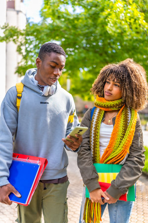 Vertical photo of two multi-ethnic students using mobile phone while walking along the university campusの写真素材