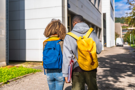 Rear view of two multi-ethnic students walking along the university campus