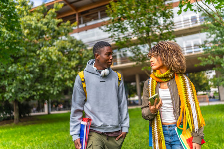 Frontal view of two multiethnic students chatting and using mobile walking out the universityの写真素材