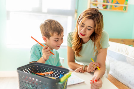 Smiling blonde boy and his young mother coloring at home togetherの写真素材