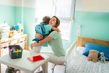 Tender mother embracing her son before going to school sitting on the kids bedroomの写真素材