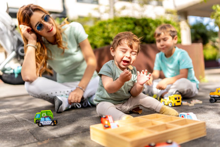 Young mother with baby and son playing sitting in a parkの写真素材