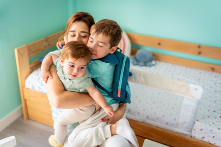 Happy family of three. Mother embracing boy and baby sitting in the bedroomの写真素材
