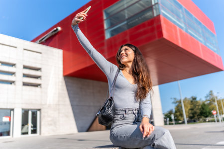 Woman smiling taking a selfie with smartphone sitting on concrete bench in the cityの写真素材