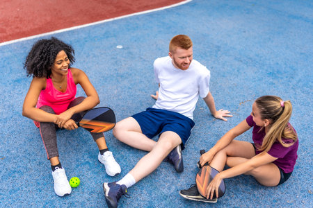 Multi-ethnic friends sitting on the ground relaxing and talking in a pickelball courtの写真素材