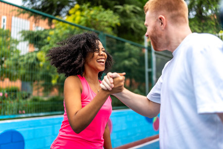 Happy multi-ethnic couple celebrating victory during pickleball match in an outdoor court