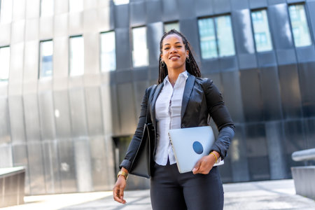Professional young latin businesswoman standing carrying laptop in the city next to a modern financial buildingの写真素材