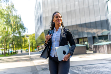 Confident latin businesswoman walking out the office carrying laptop along the cityの写真素材