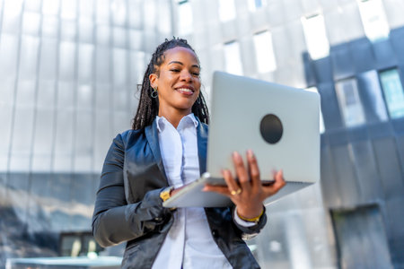 Portrait of a young successful latin businesswoman holding a laptop standing outside a financial buildingの写真素材