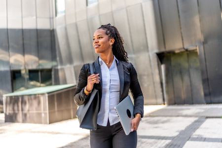 Portrait of a latin businesswoman walking distracted carrying laptop in the city next to a modern buildingの写真素材