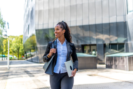 Pretty latin businesswoman walking holding laptop and handbag in a financial districtの写真素材