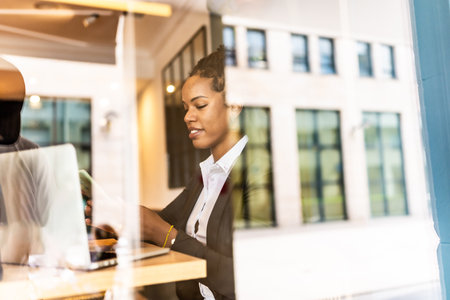 Views from outside the window of a latin businesswoman using smartphone working in a cafeteriaの写真素材